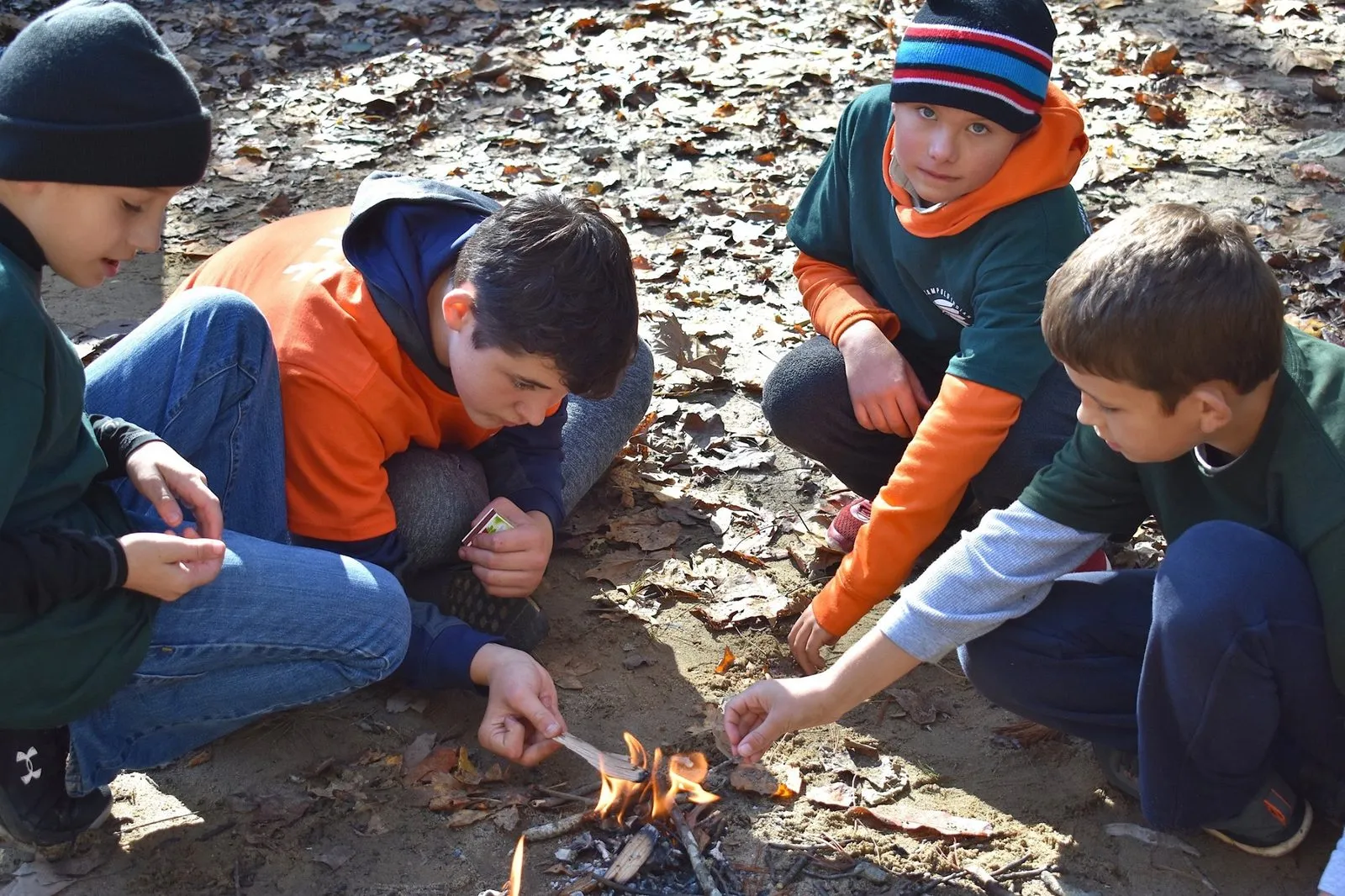 Five Cub Scouts kneeling in the leaves around the small campfire they just lit
