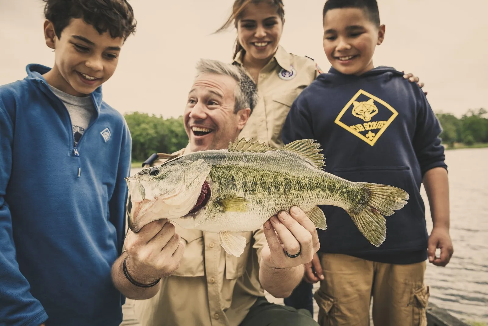 A Scout leader and three Cub Scouts grinning behind a largemouth bass