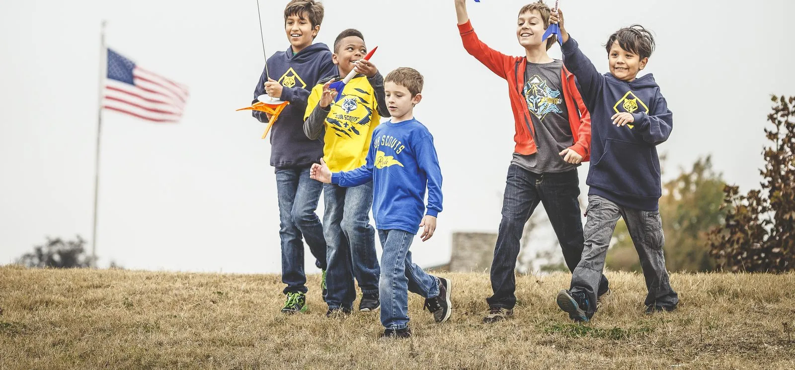 Cub Scouts walking across a field carrying model rockets they built